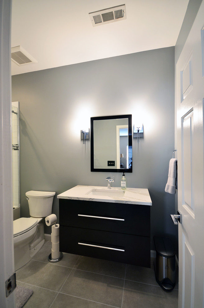 Mid-sized modern kids bathroom in Charlotte with flat-panel cabinets, black cabinets, an alcove tub, a shower/bathtub combo, a two-piece toilet, white tile, porcelain tile, blue walls, ceramic floors, an undermount sink, engineered quartz benchtops, grey floor and a sliding shower screen.