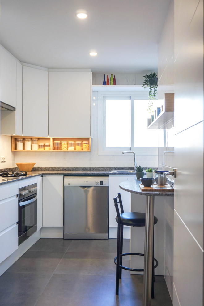 This is an example of a medium sized contemporary l-shaped enclosed kitchen in Barcelona with a double-bowl sink, flat-panel cabinets, white cabinets, marble worktops, white splashback, ceramic splashback, stainless steel appliances, porcelain flooring, a breakfast bar, black floors and black worktops.