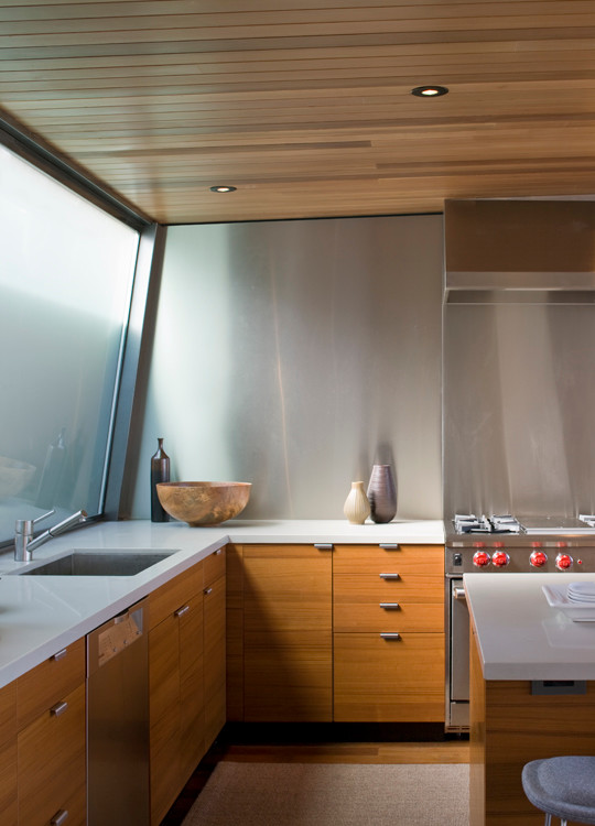 Mid-sized modern l-shaped eat-in kitchen in San Francisco with an undermount sink, flat-panel cabinets, medium wood cabinets, solid surface benchtops, metallic splashback, metal splashback, stainless steel appliances, medium hardwood floors and with island.