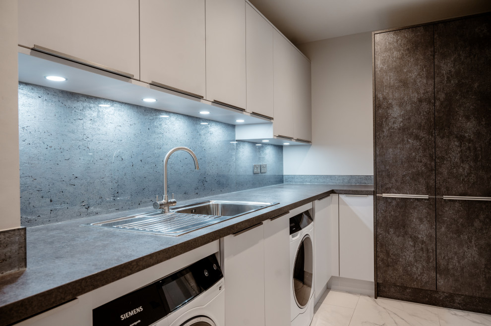 Design ideas for a large contemporary l-shaped open plan kitchen in Surrey with an integrated sink, flat-panel cabinets, grey cabinets, quartzite benchtops, blue splashback, glass sheet splashback, panelled appliances, porcelain floors, with island, white floor and white benchtop.