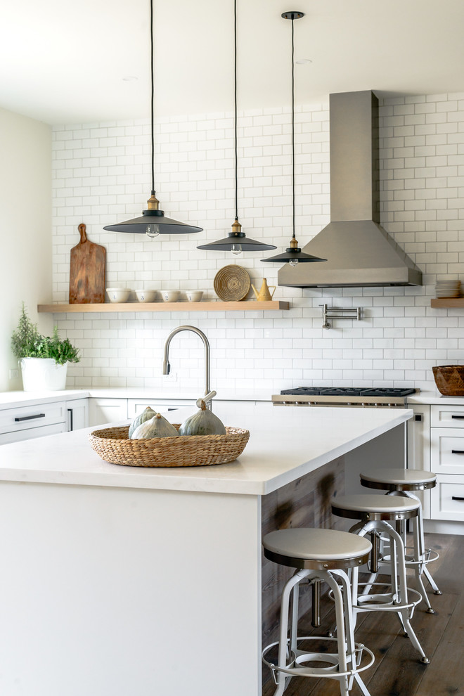 Large transitional l-shaped kitchen in Toronto with recessed-panel cabinets, white cabinets, white splashback, subway tile splashback, stainless steel appliances, with island and dark hardwood floors.