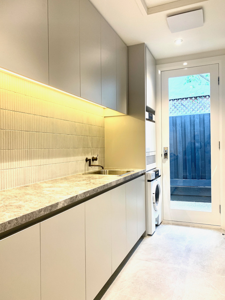 Mid-sized traditional single-wall dedicated laundry room in Melbourne with a drop-in sink, shaker cabinets, grey cabinets, white walls, porcelain floors, a stacked washer and dryer, grey floor and multi-coloured benchtop.