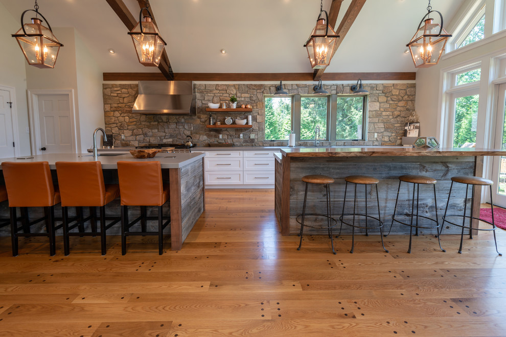 This is an example of a large country single-wall kitchen in Philadelphia with an undermount sink, flat-panel cabinets, white cabinets, quartzite benchtops, stone tile splashback, stainless steel appliances, medium hardwood floors, multiple islands, brown floor and grey benchtop.