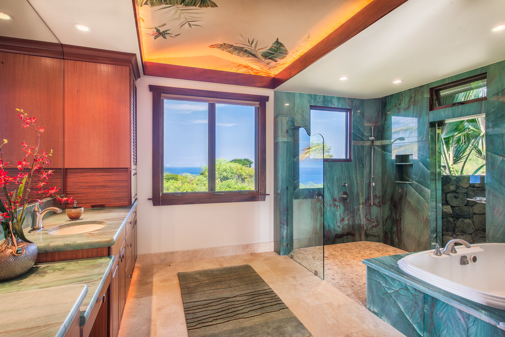 Inspiration for a large tropical master bathroom in Hawaii with louvered cabinets, medium wood cabinets, a drop-in tub, an open shower, a one-piece toilet, blue tile, pebble tile, beige walls, limestone floors, an undermount sink and granite benchtops.
