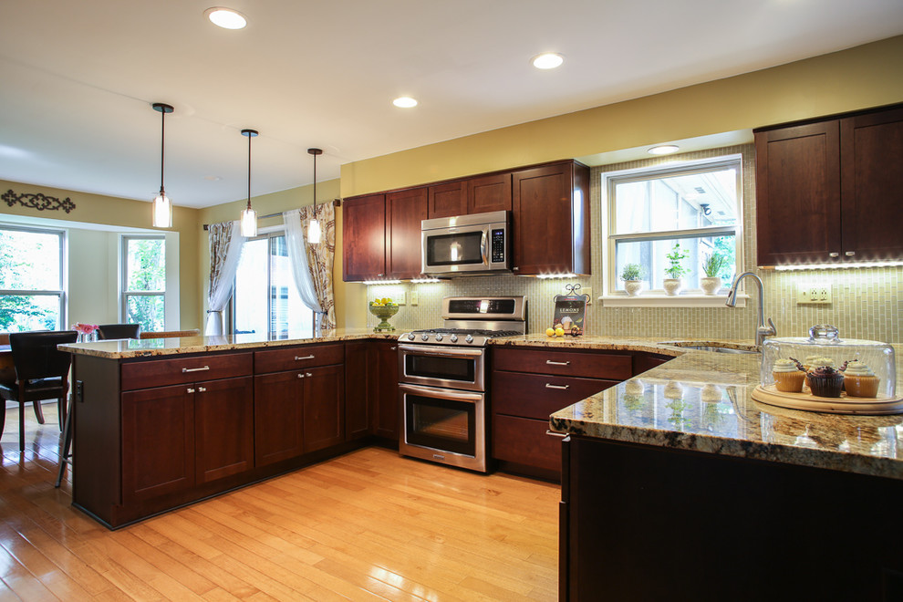 Transitional medium tone wood floor kitchen photo with an undermount sink, shaker cabinets, dark wood cabinets, granite countertops, white backsplash, glass tile backsplash and stainless steel appliances