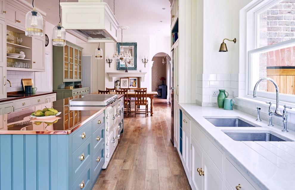 Photo of a large traditional galley eat-in kitchen in London with a double-bowl sink, recessed-panel cabinets, medium hardwood floors, with island and brown floor.