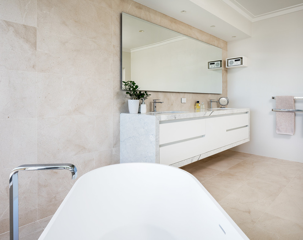 Photo of a large contemporary master bathroom in Perth with a freestanding tub, an open shower, porcelain tile, beige walls, marble floors, a wall-mount sink, marble benchtops, beige floor, a hinged shower door and white benchtops.
