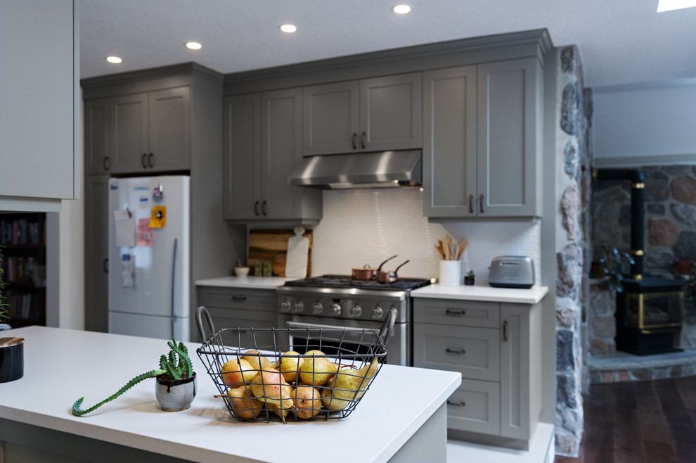 Large transitional l-shaped dark wood floor and brown floor enclosed kitchen photo in Toronto with a farmhouse sink, shaker cabinets, gray cabinets, quartz countertops, white backsplash, porcelain backsplash, stainless steel appliances and no island