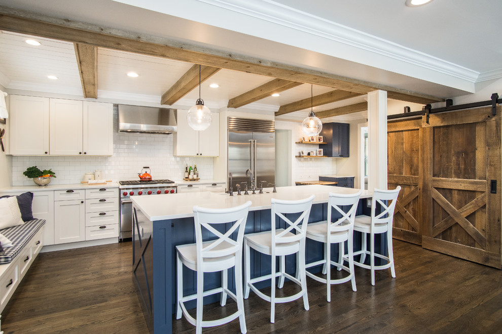 Inspiration for a cottage l-shaped dark wood floor and brown floor enclosed kitchen remodel in Chicago with a farmhouse sink, shaker cabinets, white cabinets, quartzite countertops, white backsplash, ceramic backsplash, stainless steel appliances, an island and white countertops