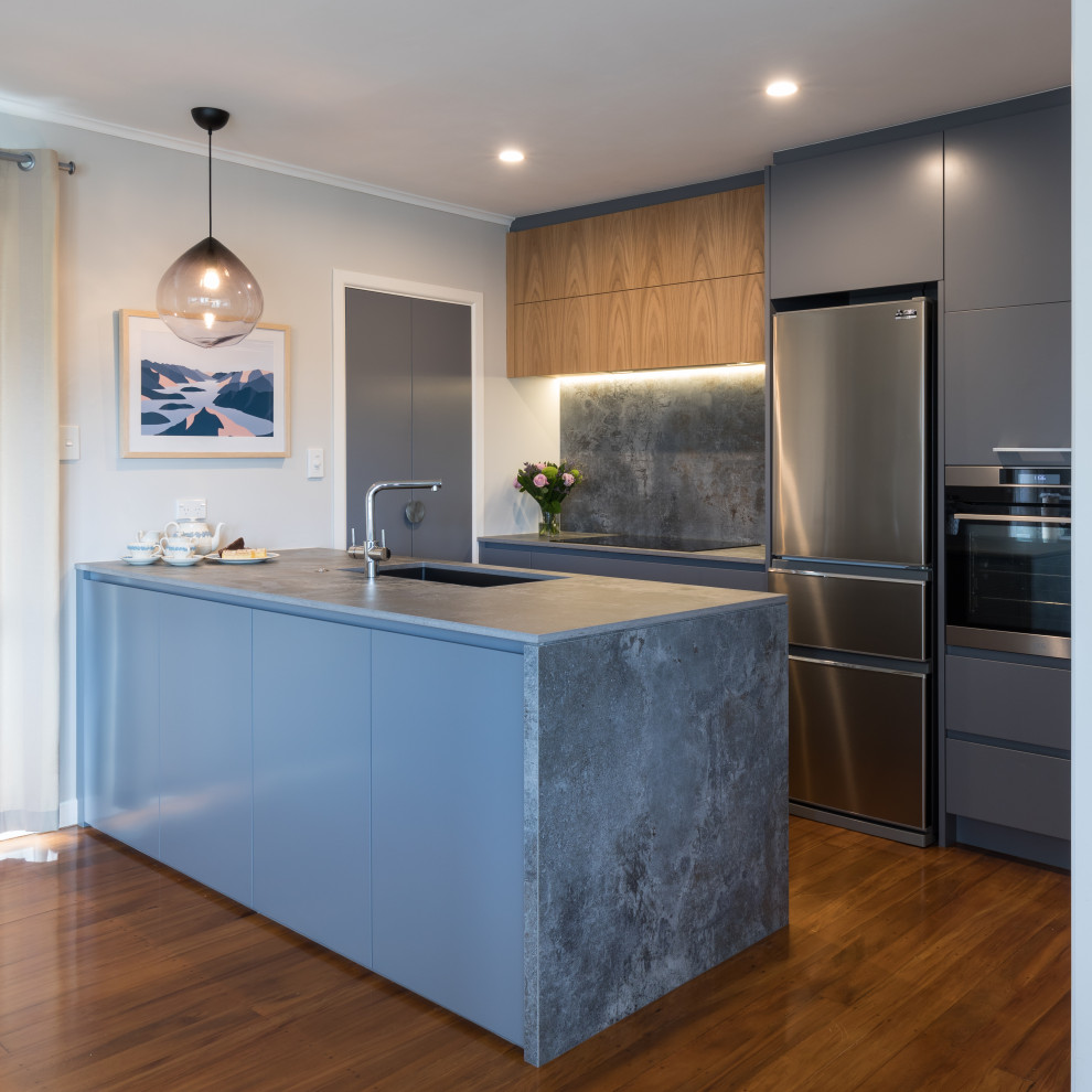 Small contemporary galley eat-in kitchen in Auckland with a double-bowl sink, flat-panel cabinets, grey cabinets, grey splashback, porcelain splashback, black appliances, light hardwood floors, a peninsula, brown floor and grey benchtop.