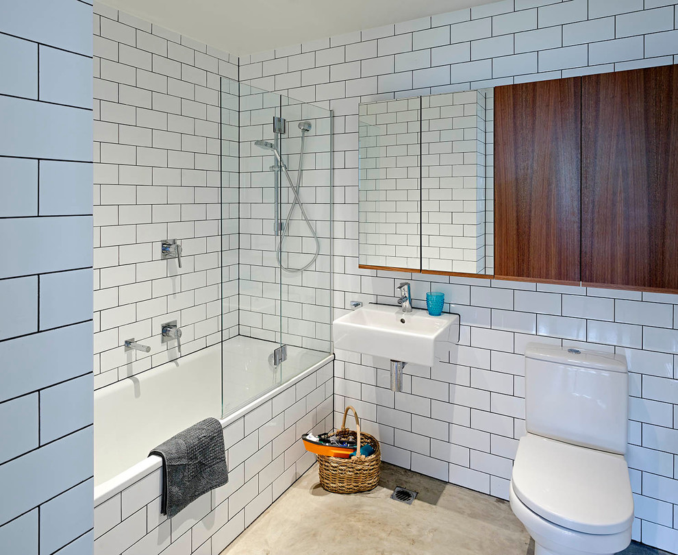 Design ideas for a mid-sized contemporary bathroom in Brisbane with dark wood cabinets, a drop-in tub, a shower/bathtub combo, a one-piece toilet, white tile, ceramic tile, concrete floors and a wall-mount sink.