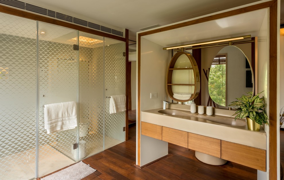 Inspiration for an asian master bathroom in Pune with flat-panel cabinets, medium wood cabinets, an alcove shower, beige tile, beige walls, dark hardwood floors, an integrated sink, brown floor, a hinged shower door and beige benchtops.