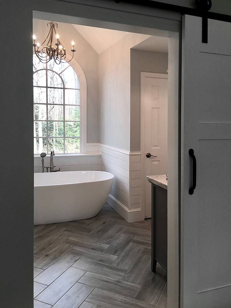 This is an example of a mid-sized country master bathroom in Atlanta with shaker cabinets, grey cabinets, a freestanding tub, a corner shower, a two-piece toilet, white tile, ceramic tile, grey walls, ceramic floors, an undermount sink, marble benchtops, grey floor and a hinged shower door.