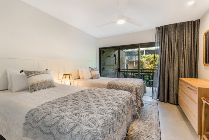 サンシャインコーストにある中くらいなビーチスタイルのおしゃれな客用寝室 (白い壁、セラミックタイルの床、ベージュの床、ベッド下のラグ、白い天井) のインテリア