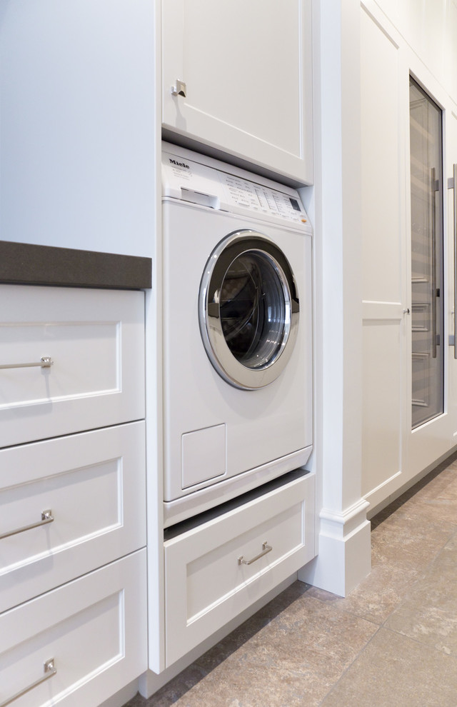 Photo of a large traditional galley utility room in Sydney with an undermount sink, shaker cabinets, white cabinets, quartz benchtops, white walls, travertine floors and a stacked washer and dryer.