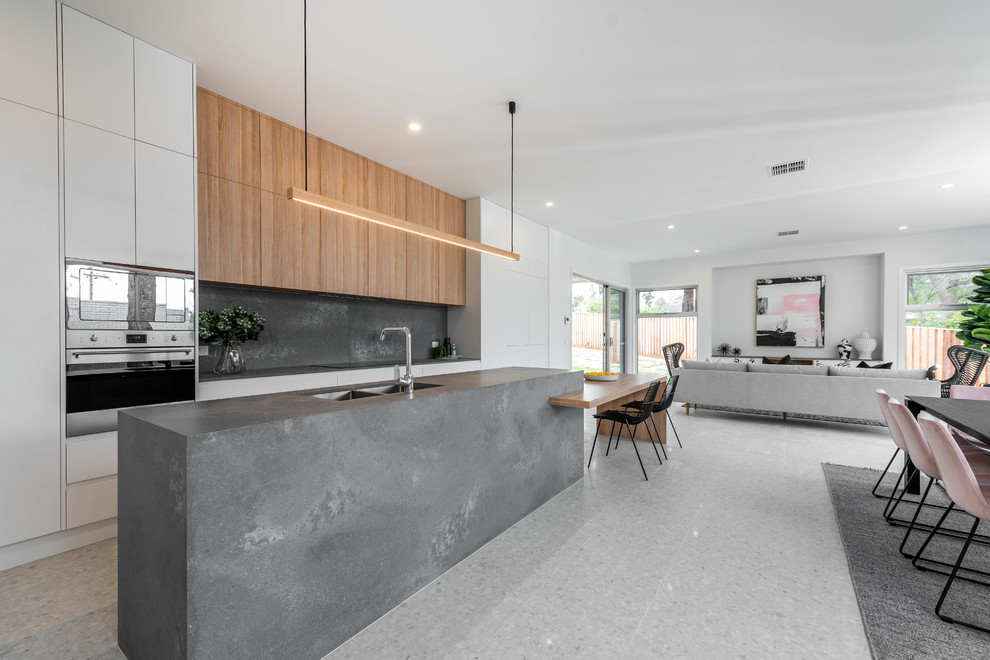 Design ideas for a contemporary galley open plan kitchen in Canberra - Queanbeyan with a double-bowl sink, flat-panel cabinets, white cabinets, grey splashback, stone slab splashback, stainless steel appliances, with island, grey benchtop and grey floor.