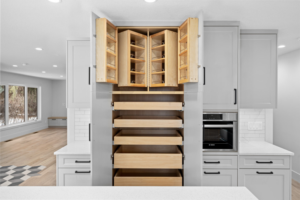 Inspiration for a small transitional l-shaped open concept kitchen remodel in Calgary with flat-panel cabinets, light wood cabinets, quartz countertops, white backsplash, ceramic backsplash, stainless steel appliances, an island and white countertops