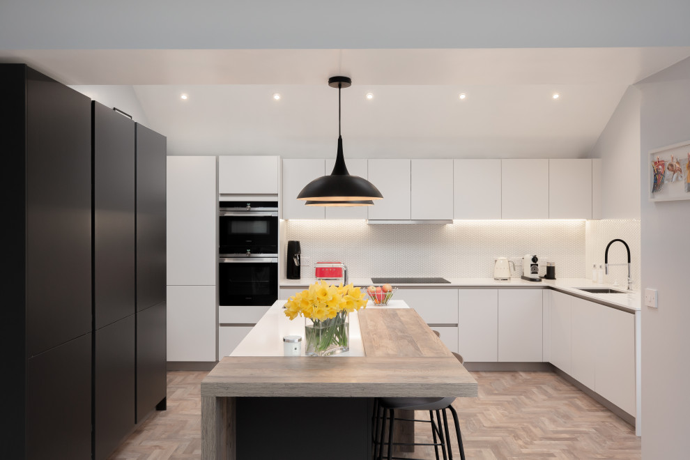 This is an example of a medium sized contemporary u-shaped kitchen in Other with a single-bowl sink, flat-panel cabinets, white cabinets, quartz worktops, white splashback, ceramic splashback, black appliances, light hardwood flooring, an island, white worktops and beige floors.