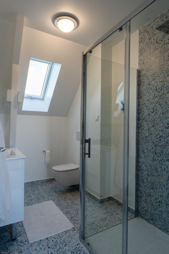 This is an example of a small eclectic 3/4 bathroom in Paris with beaded inset cabinets, white cabinets, an alcove shower, a wall-mount toilet, multi-coloured tile, ceramic tile, white walls, ceramic floors, a drop-in sink, laminate benchtops, grey floor, a sliding shower screen, white benchtops, a single vanity and a floating vanity.