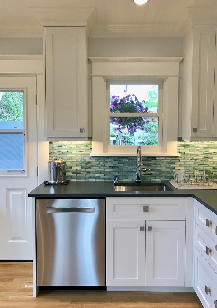 Inspiration for a small arts and crafts l-shaped eat-in kitchen in Seattle with an undermount sink, shaker cabinets, white cabinets, solid surface benchtops, blue splashback, glass tile splashback, stainless steel appliances, light hardwood floors, yellow floor and grey benchtop.