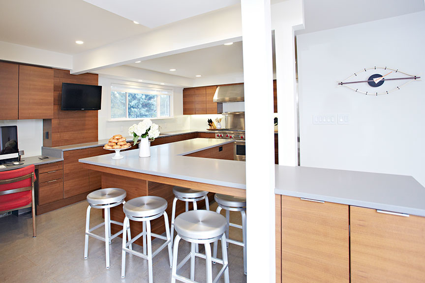 This is an example of a mid-sized contemporary l-shaped eat-in kitchen in Edmonton with beige splashback, glass tile splashback, an undermount sink, flat-panel cabinets, medium wood cabinets, solid surface benchtops, stainless steel appliances, travertine floors, with island and beige floor.