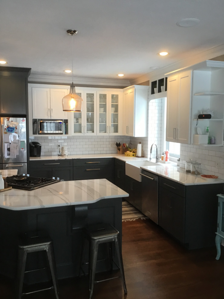 Eat-in kitchen - mid-sized transitional l-shaped dark wood floor and red floor eat-in kitchen idea with a farmhouse sink, recessed-panel cabinets, gray cabinets, stainless steel appliances, an island, white countertops, quartz countertops, white backsplash and subway tile backsplash