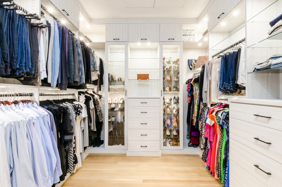 Photo of an expansive gender-neutral walk-in wardrobe in New York with light wood cabinets and light hardwood floors.