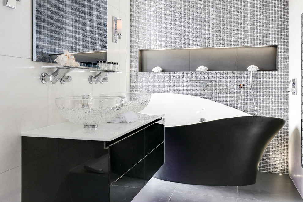 Design ideas for a contemporary master bathroom in London with flat-panel cabinets, a freestanding tub, mosaic tile, a vessel sink, grey floor, black cabinets and multi-coloured tile.