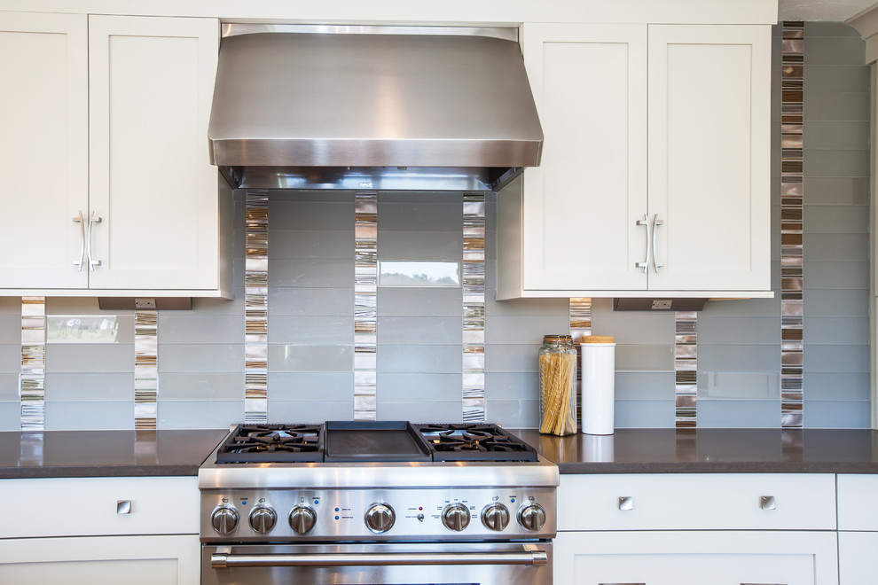 Inspiration for a large transitional l-shaped medium tone wood floor eat-in kitchen remodel in Boston with an undermount sink, shaker cabinets, white cabinets, quartz countertops, gray backsplash, glass sheet backsplash, stainless steel appliances and an island