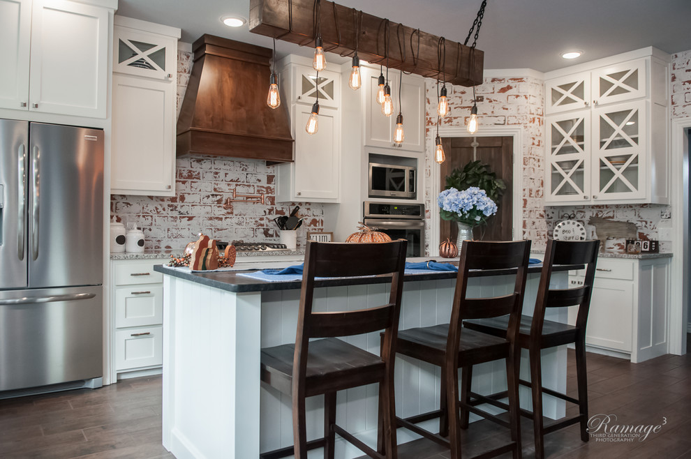 Large transitional u-shaped open plan kitchen in Other with a farmhouse sink, shaker cabinets, white cabinets, granite benchtops, brick splashback, stainless steel appliances, with island, brown floor and grey benchtop.