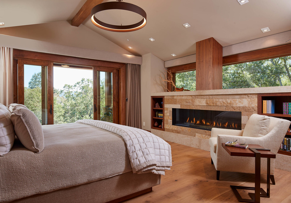 Design ideas for a country bedroom in San Francisco with beige walls, medium hardwood floors, a ribbon fireplace, a stone fireplace surround and brown floor.