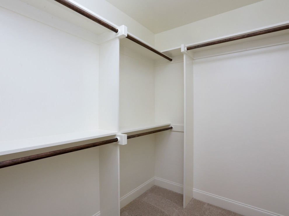 Large traditional gender-neutral walk-in wardrobe in Raleigh with white cabinets and carpet.