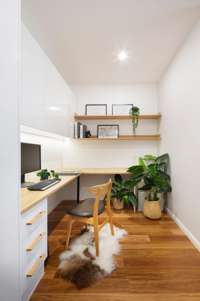 Aménagement d'un petit bureau avec un mur blanc, un sol en bois brun et un bureau intégré.