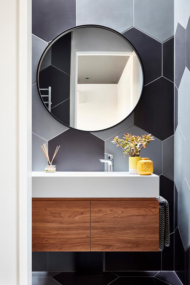 This is an example of a small contemporary bathroom in Melbourne with flat-panel cabinets, medium wood cabinets, gray tile, porcelain tile, an integrated sink, solid surface benchtops and white benchtops.