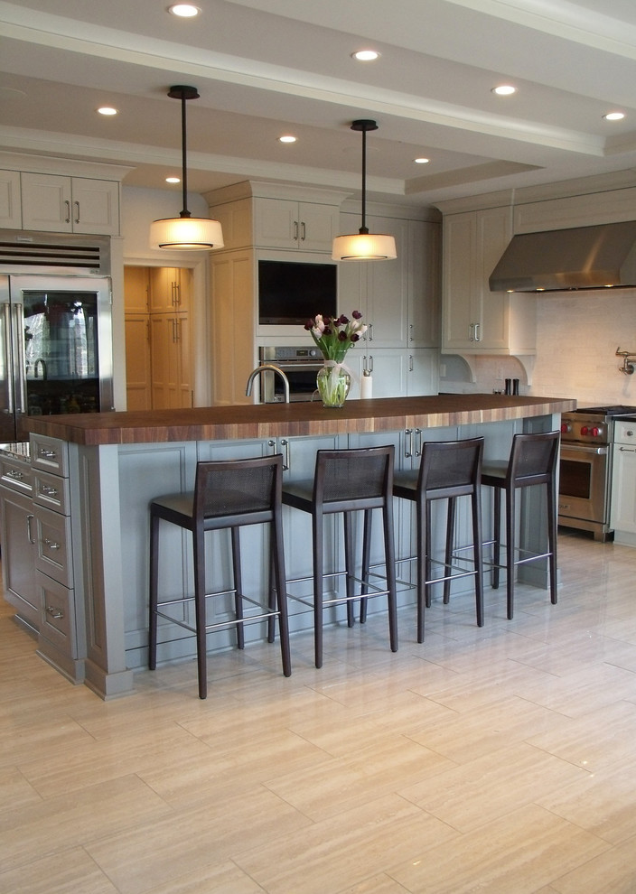 Mid-sized transitional l-shaped porcelain tile and beige floor enclosed kitchen photo with an undermount sink, recessed-panel cabinets, white cabinets, wood countertops, white backsplash, subway tile backsplash, stainless steel appliances and an island