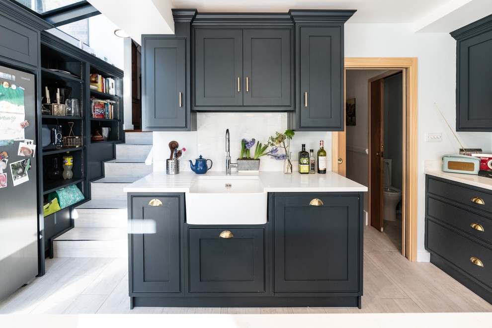 Design ideas for a small contemporary u-shaped kitchen in London with a farmhouse sink, recessed-panel cabinets, blue cabinets, quartzite benchtops, white splashback, with island and white benchtop.