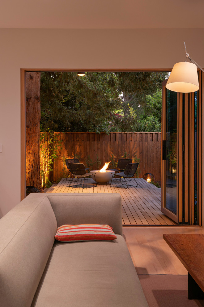 Aménagement d'un petit jardin arrière moderne avec un foyer extérieur, une exposition partiellement ombragée, une terrasse en bois et une clôture en bois.