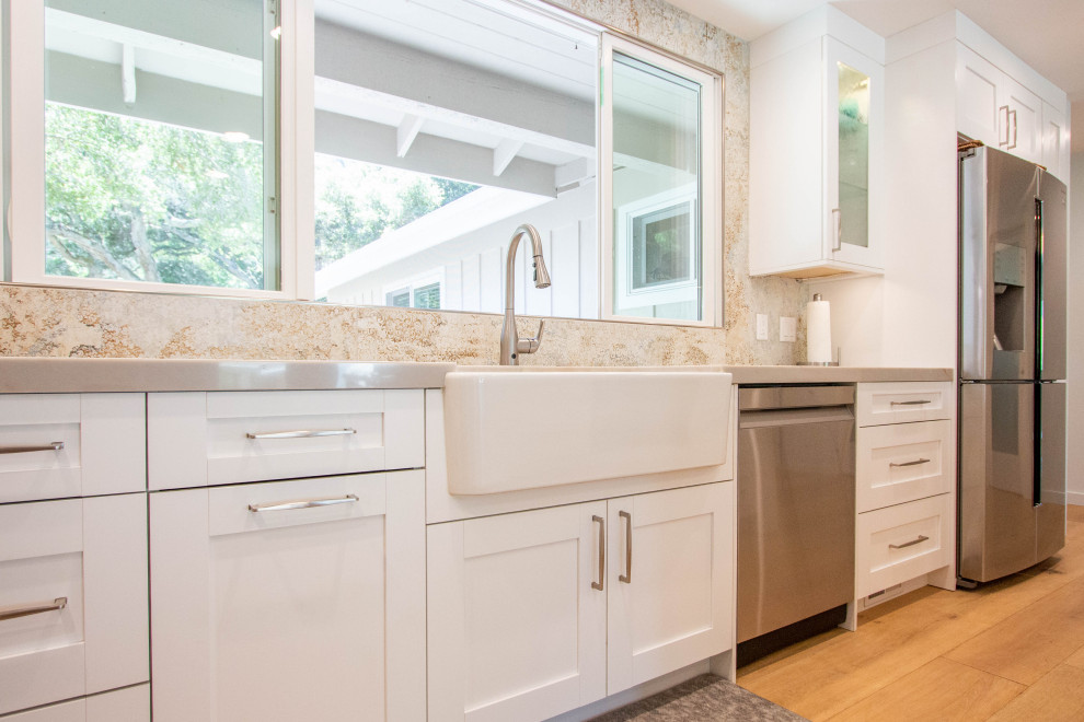 Eat-in kitchen - transitional l-shaped light wood floor and brown floor eat-in kitchen idea with a farmhouse sink, shaker cabinets, white cabinets, quartz countertops, porcelain backsplash, stainless steel appliances and an island