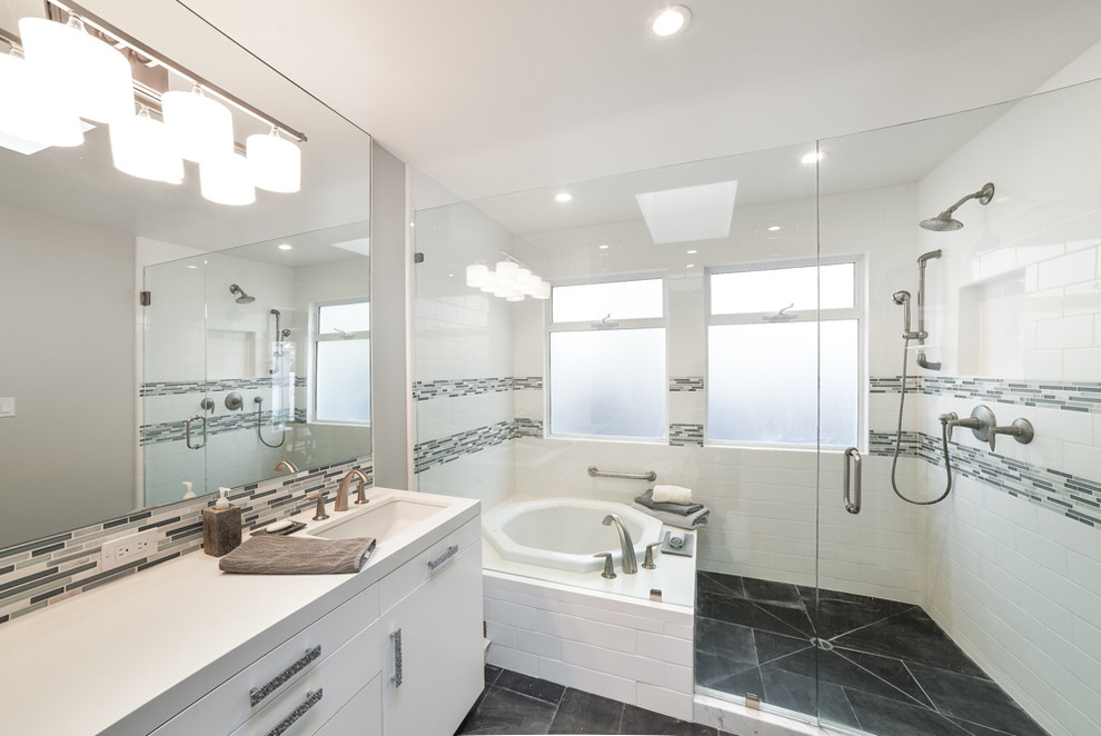 Mid-sized transitional master bathroom in Los Angeles with flat-panel cabinets, white cabinets, a drop-in tub, an alcove shower, black and white tile, gray tile, matchstick tile, white walls, an undermount sink, solid surface benchtops, slate floors, black floor and a hinged shower door.