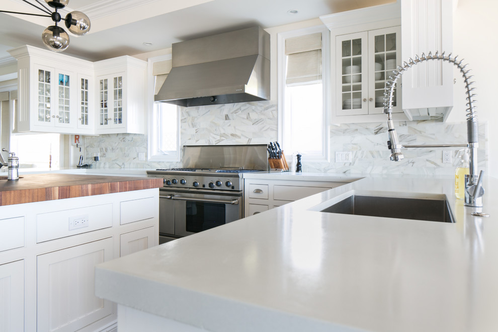 This is an example of a mid-sized u-shaped eat-in kitchen in Orange County with a single-bowl sink, glass-front cabinets, white cabinets, concrete benchtops, white splashback, stone tile splashback, stainless steel appliances, with island and medium hardwood floors.