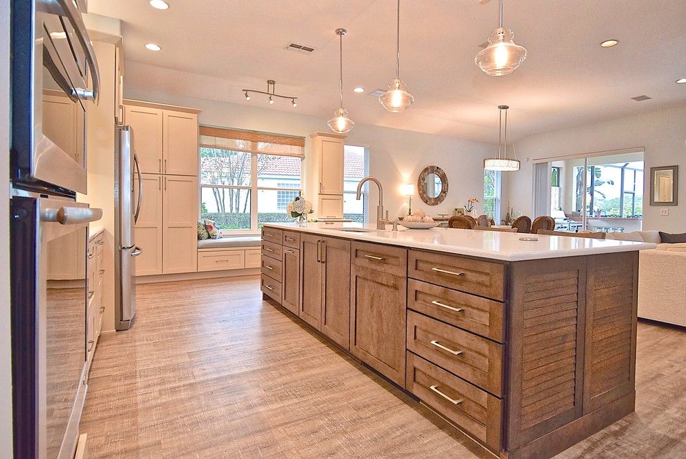 This is an example of an expansive transitional open plan kitchen in Tampa with an undermount sink, shaker cabinets, brown cabinets, quartz benchtops, stainless steel appliances, vinyl floors, with island and brown floor.