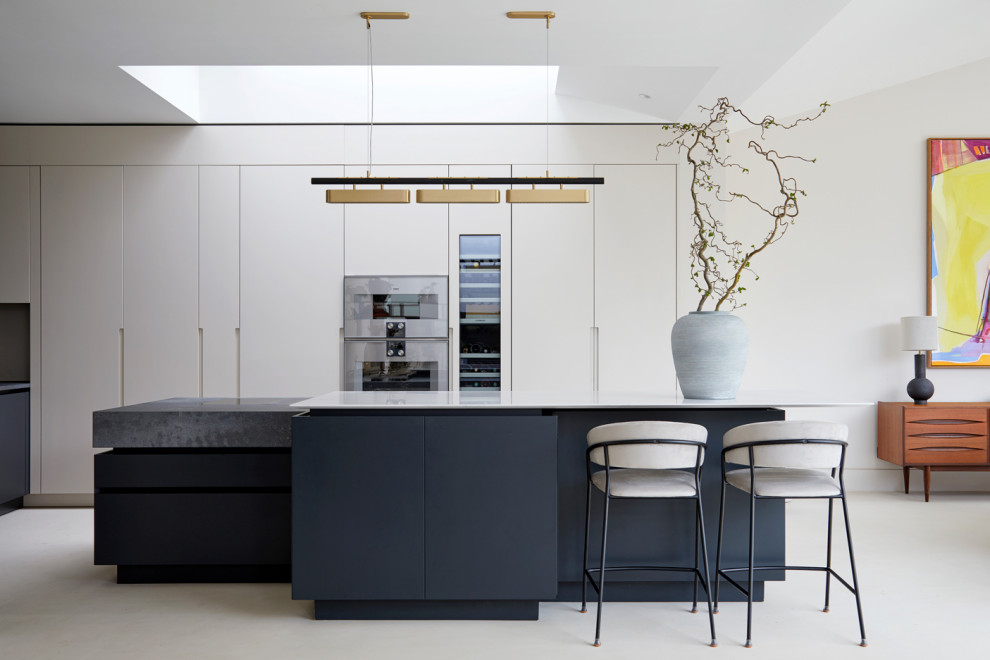 Inspiration for an expansive contemporary open plan kitchen in London with a drop-in sink, flat-panel cabinets, beige cabinets, solid surface benchtops, black appliances, concrete floors, multiple islands, beige floor and grey benchtop.