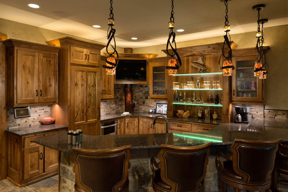Inspiration for a large country u-shaped seated home bar in Kansas City with an undermount sink, glass-front cabinets, medium wood cabinets, granite benchtops, grey splashback, stone tile splashback and slate floors.