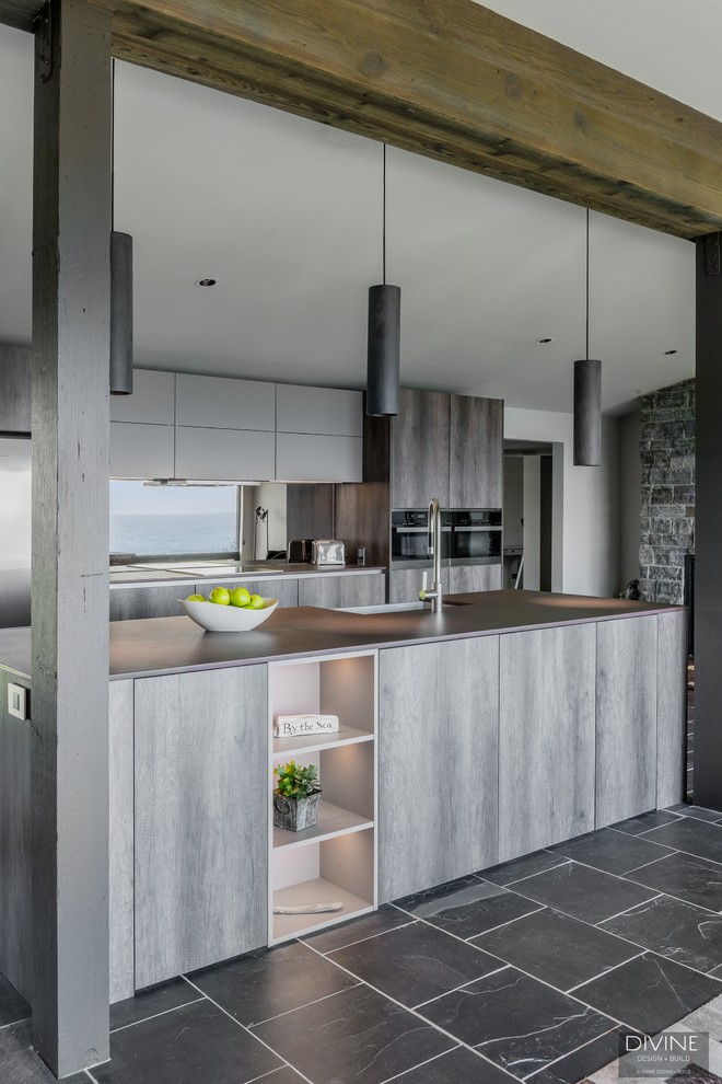 Large eclectic single-wall open plan kitchen in Boston with a farmhouse sink, flat-panel cabinets, dark wood cabinets, granite benchtops, metallic splashback, glass sheet splashback, stainless steel appliances, slate floors, with island, grey floor and brown benchtop.