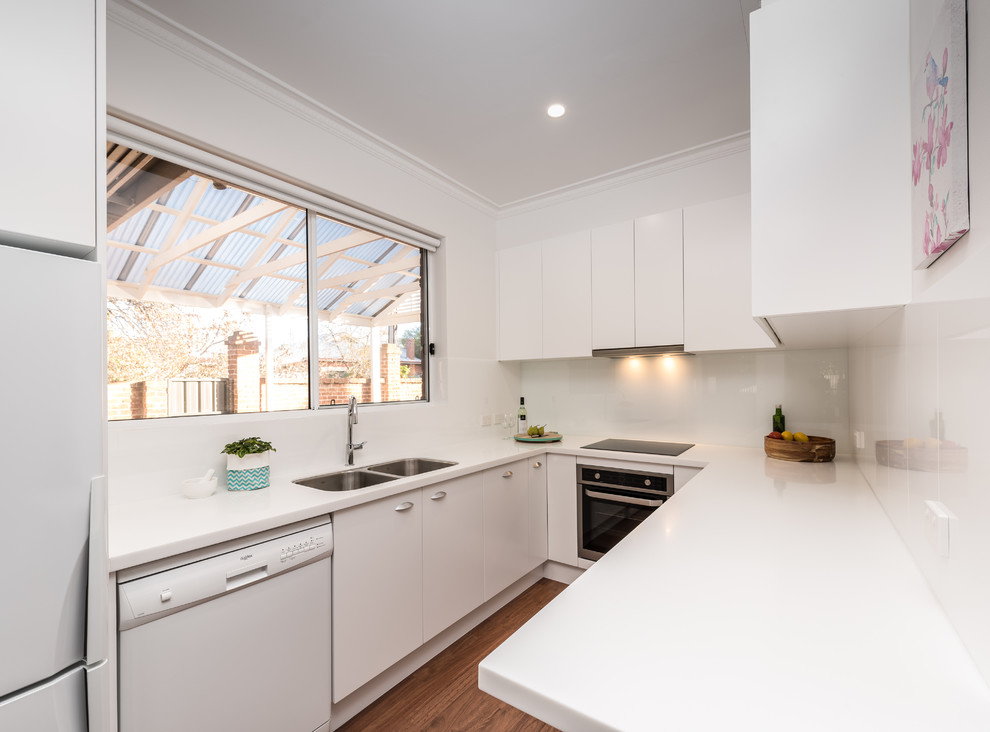 This is an example of a small contemporary u-shaped separate kitchen in Other with a double-bowl sink, white cabinets, quartz benchtops, white splashback, glass sheet splashback, white appliances and medium hardwood floors.