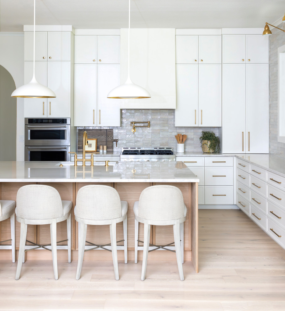 Kitchen - transitional l-shaped light wood floor and beige floor kitchen idea in Austin with an undermount sink, recessed-panel cabinets, white cabinets, gray backsplash, stainless steel appliances, an island and gray countertops