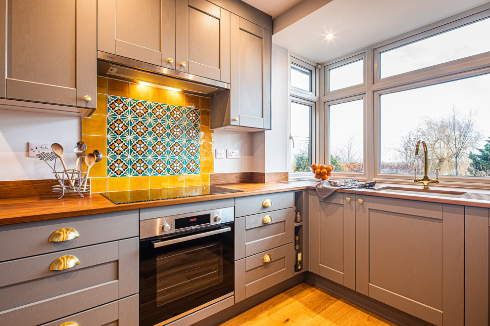 Photo of a medium sized eclectic u-shaped kitchen/diner in Other with a submerged sink, shaker cabinets, grey cabinets, wood worktops, yellow splashback, terracotta splashback, a breakfast bar, brown floors and brown worktops.