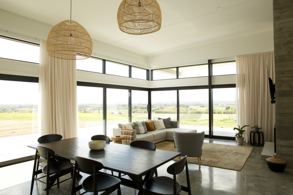 Réalisation d'une grande salle à manger ouverte sur la cuisine minimaliste avec un mur blanc, sol en béton ciré, un manteau de cheminée en béton, un sol gris et un plafond voûté.