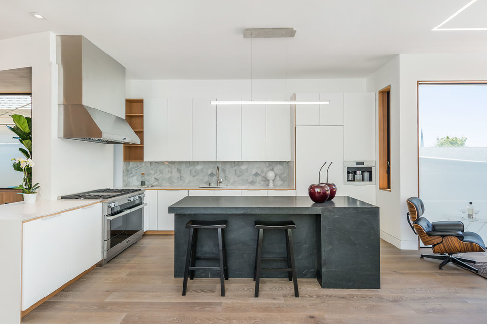 Photo of a mid-sized contemporary l-shaped open plan kitchen in San Francisco with flat-panel cabinets, white cabinets, grey splashback, stainless steel appliances, medium hardwood floors, with island, brown floor, beige benchtop, solid surface benchtops and marble splashback.