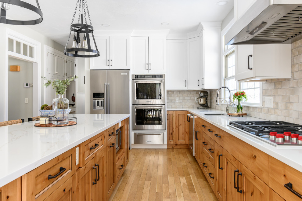 Large farmhouse l-shaped light wood floor and brown floor eat-in kitchen photo in Boston with an undermount sink, recessed-panel cabinets, white cabinets, quartz countertops, beige backsplash, ceramic backsplash, stainless steel appliances, an island and white countertops